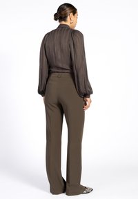 Bruine doorschijnende blouse met verticale strepen, lange pofmouwen en op maat gemaakte bruine broeken. De outfit heeft unieke accenten aan de zoom van de blouse.