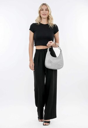 Bolso gris texturizado con forma curvada y acentos decorativos, combinado con una blusa negra corta y pantalones negros de pierna ancha.