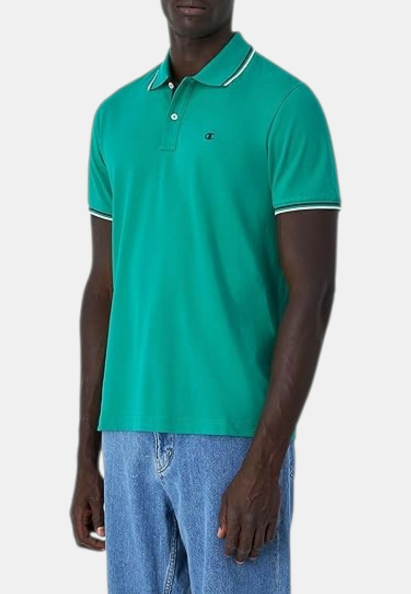 Hombre con una camiseta polo verde de manga corta con ribete blanco en el cuello y las mangas, combinada con vaqueros azules.