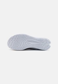 Suela blanca de zapatilla Under Armour con un patrón de tracción texturizado y estriado, y el logo cerca del talón, sobre un fondo blanco liso.