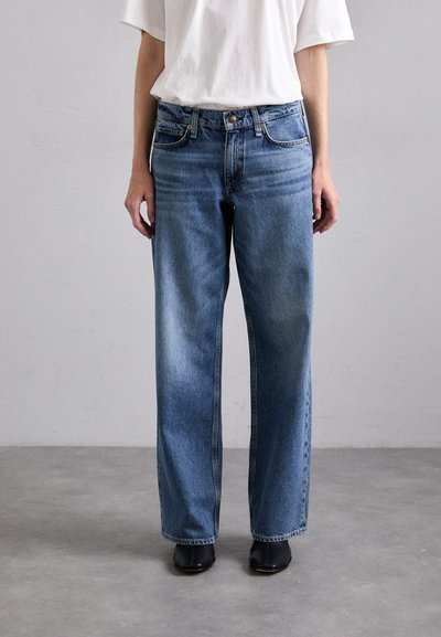 Jean en denim bleu clair, coupe large avec une finition délavée. Dispose de cinq poches, d'une fermeture boutonnée et de passants de ceinture. Porté avec un t-shirt blanc.
