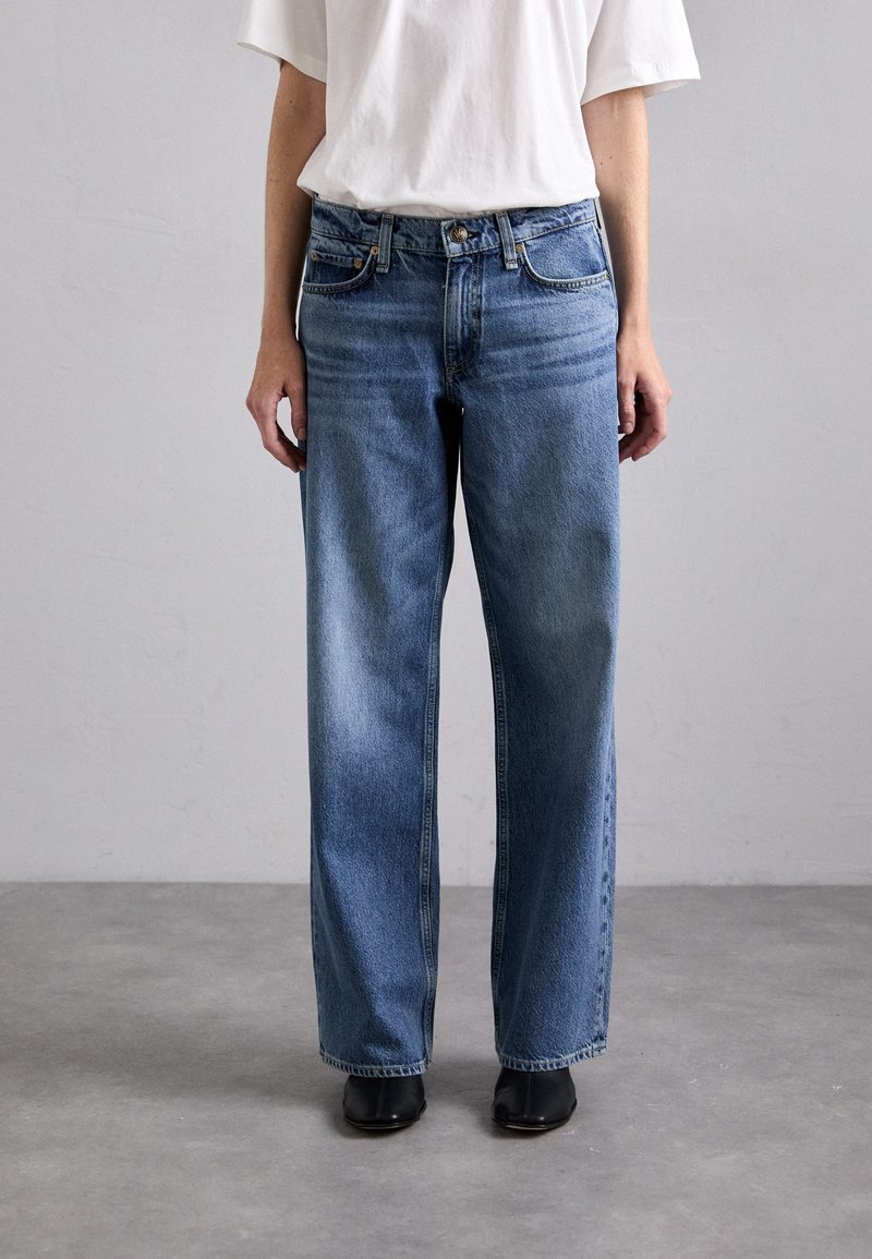 Light blue, wide-leg denim jeans with a faded finish. Features five pockets, a button closure, and belt loops. Worn with a white t-shirt.