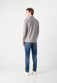 Light grey long-sleeve shirt with a collar, paired with blue jeans. Model is facing away, showcasing shirt's back design and casual fit.