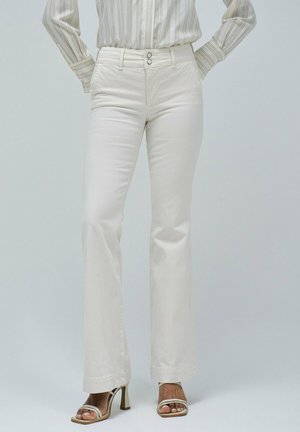 Pantalones acampanados blancos hechos de una tela suave, con una cintura alta, cierre de dos botones y un dobladillo pulido. Combinados con sandalias plateadas.