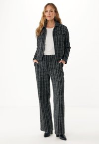 Completo in tweed a scacchi bianco e nero con giacca aderente e pantaloni a gamba larga, abbinato a una maglietta bianca e stivali neri alla caviglia.