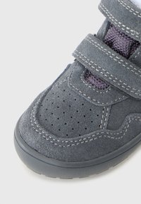 Hallukad hallist sametist, millel on kaks laia Velcro rihma, perforeritud varvas, kontrastne piste ja tekstuuriga kangast detailid. Nähtav kummist tald.