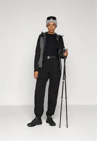 Kültéri ruházati szett fekete dzsekivel, szürke díszítésekkel és sötét nadrággal. Kiegészítők között található egy szürke sapka és túrabotok.