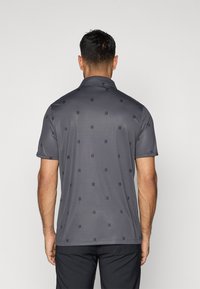 Polo gris avec un motif discret sur l'ensemble, des accents noirs, des manches courtes et un col. Tissu lisse et léger.