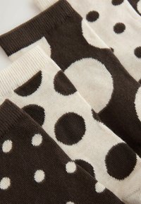 Rudos ir kreminės spalvų kojinės su įvairiais taškuotais raštais, įskaitant mažus ir didelius taškus, su raustytais krašteliais tekstūrai.