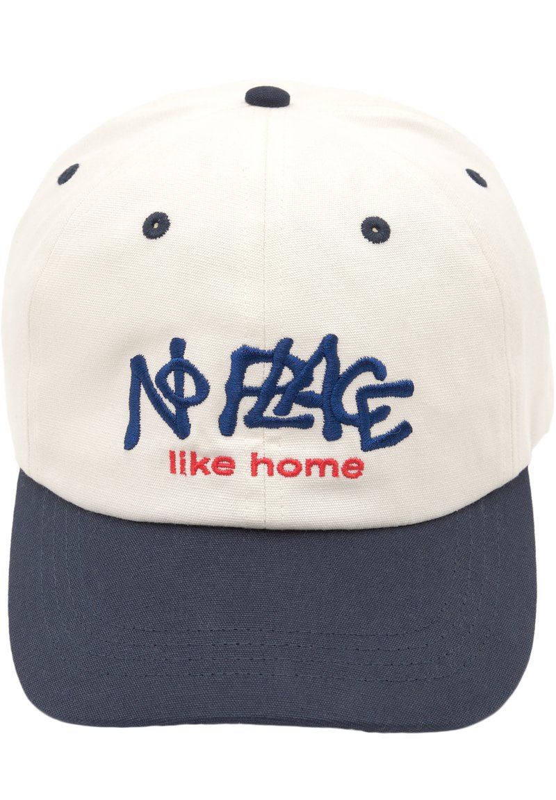 Keps med en krämfärgad front och en marinblå skärm, broderad text "NO FLAG like home" i blått och rött, strukturerad form och tygmaterial.