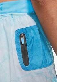 Pantalones cortos deportivos de color azul claro con un bolsillo contrastante de color azul oscuro. Con cierre con cremallera y una pequeña lengüeta azul.
