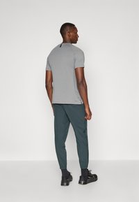 Tricou gri cu mânecă scurtă și un accent negru la gât, asortat cu pantaloni verde închis evazați și adidași negri cu detalii aurii.