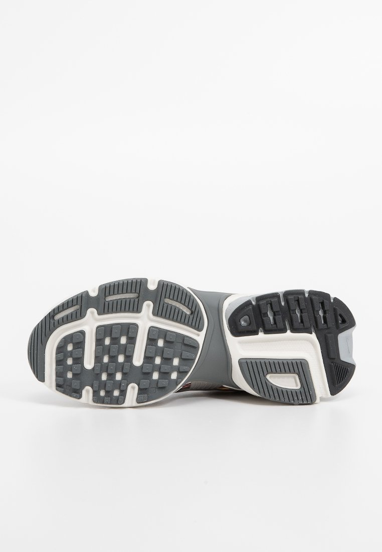 Suela de zapato deportivo gris con goma texturizada, que presenta surcos y áreas de agarre en patrón para tracción. Presencia de una entresuela blanca y acentos.