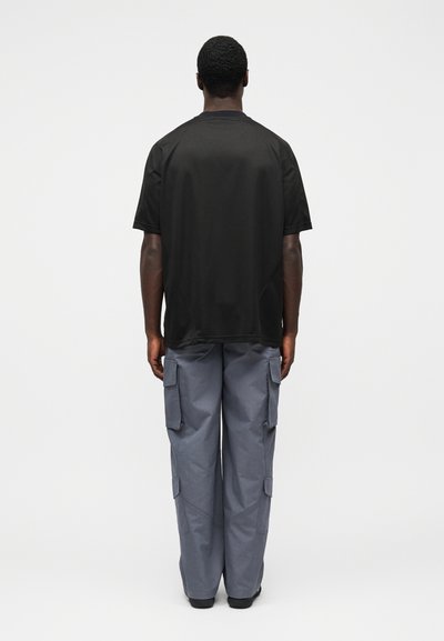 Black short-sleeve t-shirt with a round neckline, paired with gray cargo pants featuring side pockets and a relaxed fit.