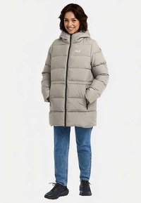 Lichtgrijze gewatteerde jas met capuchon, ritssluiting aan de voorkant en twee zijzakken. Gedragen over een blauwe spijkerbroek en zwarte schoenen, met een doorgestikte textuur.