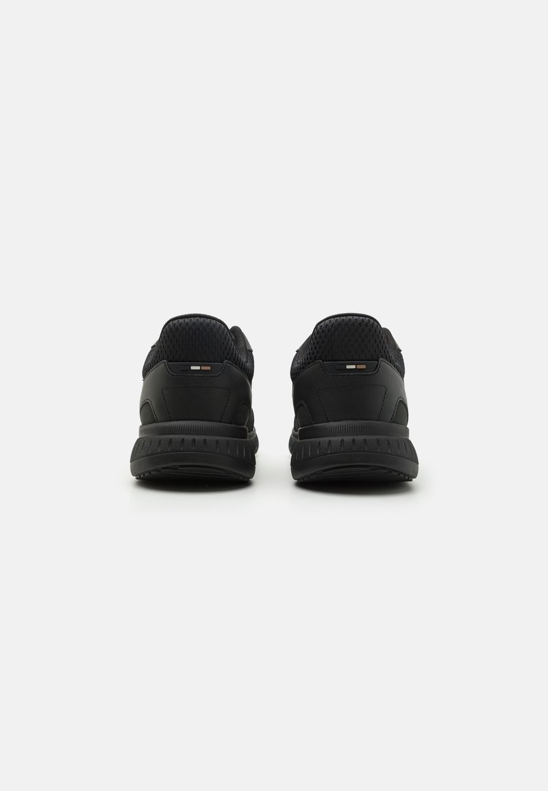 Zapatillas deportivas negras con parte superior de malla, cuello acolchado y suela de goma texturizada. Presentan acentos minimalistas y un diseño curvado.