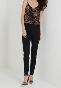Leopard print camisole top in brown tones, paired with black skinny pants, complemented by black high-heeled sandals.