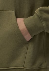 Felpa verde oliva con tasca a marsupio frontale e polsini a costine. Texture morbida con dettagli di cucitura visibili lungo le cuciture.