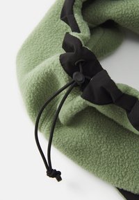 Gros plan sur un tissu en polaire vert avec un cordon noir et un arrêtoir pour un ajustement réglable.