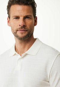 Witte polo met een structuurstof en subtiele horizontale strepen, een klassieke kraag en een knopenlijst.