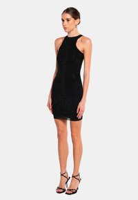 Robe noire moulante avec un col haut et un design texturé. Stylée avec des escarpins noirs à brides et accessoirisée avec de petites boucles d'oreilles.