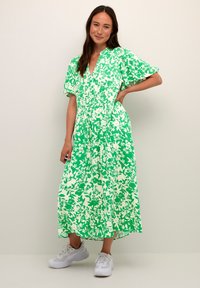 Zeleno cvetlično maxi obleko s kratkimi napihnjenimi rokavi, V-izrezom, stisnjem pasom in ohlapno silhueto, v kombinaciji z belimi športnimi copati.