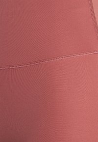 Legginsy sportowe o wysokim stanie w odcieniu przybrudzonego różu, wykonane z gładkiego, elastycznego materiału z delikatnym połyskiem oraz wzmocnionymi szwami dla zwiększenia trwałości.
