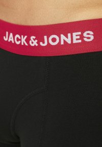 Bóxer negro con una cinturilla elástica roja que muestra el texto "JACK & JONES" en blanco. La tela parece suave con costuras visibles.