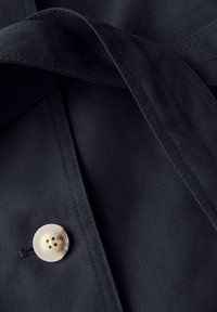 Czarna tkanina o gładkiej fakturze, z dużym beżowym guzikiem i starannie przeszytymi brzegami. Zawiera złożony kołnierzyk i krawat.