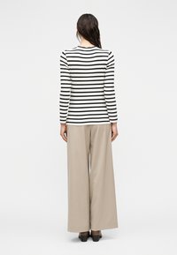 Μακρυμάνικη ριγέ μπλούζα σε μαύρο και λευκό, συνδυασμένη με μπεζ παντελόνι φαρδιάς γραμμής, με άνετη εφαρμογή και λεία υφή υφάσματος.