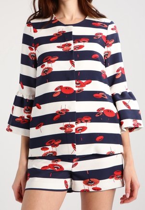Frau trägt ein marineblau-weiß breit gestreiftes Langarmoberteil und passende Shorts mit rotem Blumen-Regenschirm-Muster.