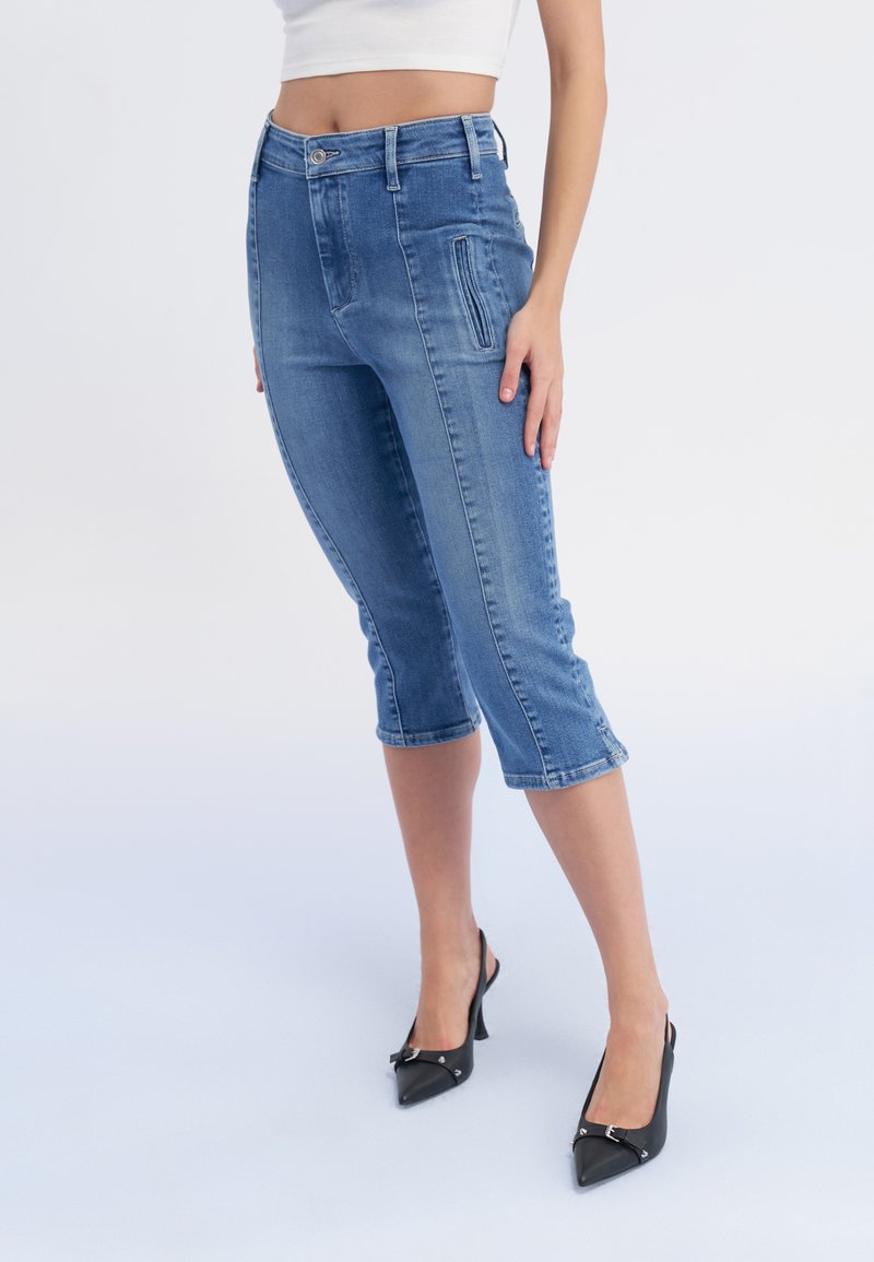 Gaiši zili denim šorti ar augstu jostasvietu, priekšējām kabatām un īsu garumu, stilizēti ar melniem siksnu papēžiem.