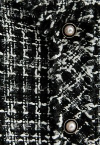 Schwarz-weißer Tweed-Stoff mit einem strukturierten, gewebten Muster. Verfügt über einen runden Perlmuttknopf mit einem goldfarbenen Rand.