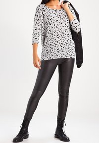 Haut gris clair avec un motif de feuilles noires, à manches trois-quarts, associé à un legging en simili cuir noir et des bottines à lacets noires.