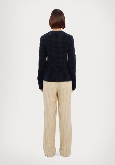 Navy textured knit sweater with long sleeves, ribbed detailing, and a fitted waist, paired with cream-striped wide-leg pants.