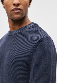 Camisola de malha azul-marinho com textura canelada, decote redondo e mangas ajustadas. Pespontes detalhados acrescentam interesse visual ao tecido.