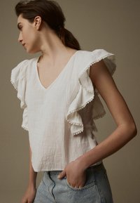 Haut en lin blanc avec un décolleté en V et des manches volantées, orné de délicates dentelles. Associé à un bas en denim bleu clair.