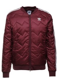 Burgundy vadderad jacka med chevronmönster, ribbat manschetter och nederkant, dragkedja fram och vita tre-strimmor på ärmarna. Adidas-logotyp på bröstet.