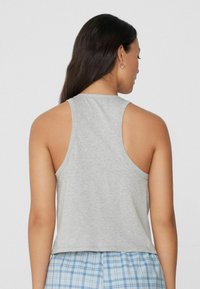 Top leggero grigio chiaro senza maniche con scollatura rotonda e vestibilità rilassata. Il tessuto sembra morbido con una leggera texture, abbinato a pantaloni a quadri.