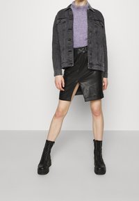 Giacca in denim nera sopra un maglione a coste viola, abbinata a una gonna in pelle nera con spacco frontale e stivali alla caviglia neri con lacci.