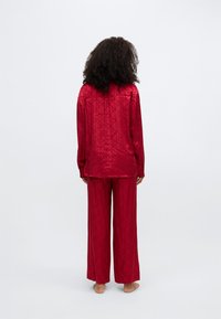 Czerwony satynowy komplet piżamowy składający się z koszuli z długim rękawem i szerokich spodni, oba z geometrycznym wzorem i gładką fakturą.