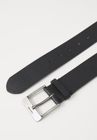 Melnas ādas josta ar teksturētu apdari, sudraba metāla sprādze un vairāki regulēšanas caurumi gar siksnu.