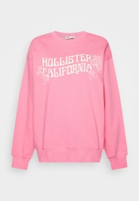 Rosa sweatshirt med rund hals, med vit text "HOLLISTER CALIFORNIA" och blommiga och svampgrafik. Mjuk bomullsblandning.