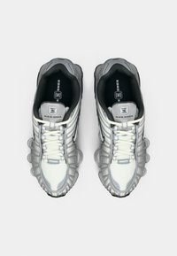 Para srebrno-białych sneakersów Nike Shox z czarnymi wkładkami, zaokrąglonym noskiem i widocznymi kolumnami amortyzacyjnymi na podeszwie, widziana z góry.