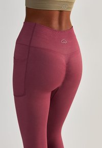 Leggings taille haute en bordeaux profond, fabriqués à partir d'un matériau extensible avec une texture lisse, dotés d'une poche latérale et d'un détail en forme de cœur.