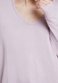 Pullover viola chiaro a scollo a V con collo e polsini a coste, caratterizzato da una texture morbida e liscia e una vestibilità comoda. La vista ravvicinata mette in evidenza i dettagli.