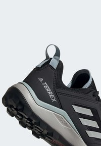 Chaussure de trail Adidas Terrex noire avec des accents gris, semelle texturée pour une meilleure adhérence et languette au talon.