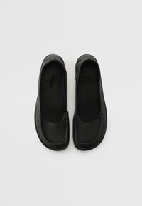Svarta slip-on skor i texturerat läder, med rundad tå och släta kanter, i en minimalistisk design utan synlig hårdvara.