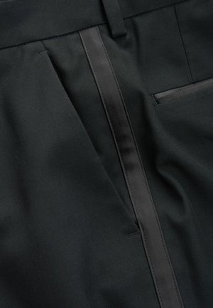 Schwarze, maßgeschneiderte Hosen zeichnen sich durch eine glatte Textur, einen schlanken Satinstreifen an der Seite und eine seitliche Tasche auf der rechten Seite aus.