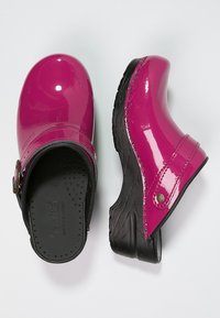 Fuchsia patent leather clogs with a black rubber base. Features adjustable buckle and perforated footbed for ventilation and comfort.